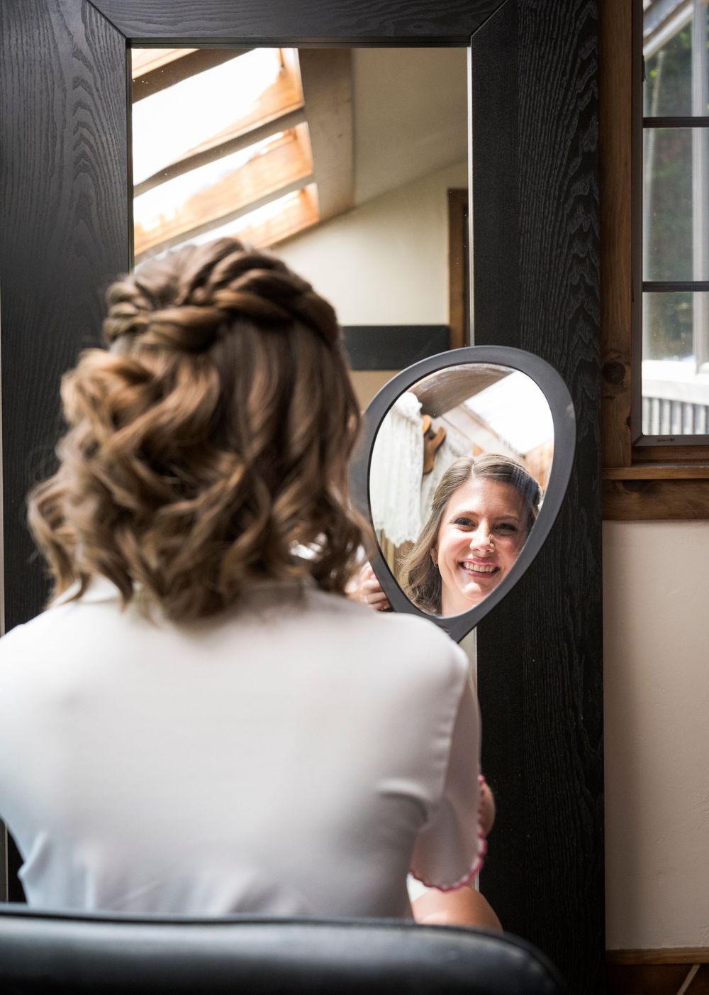 Bride admiring her elegant updo hairstyle in a handheld mirror during wedding preparations.