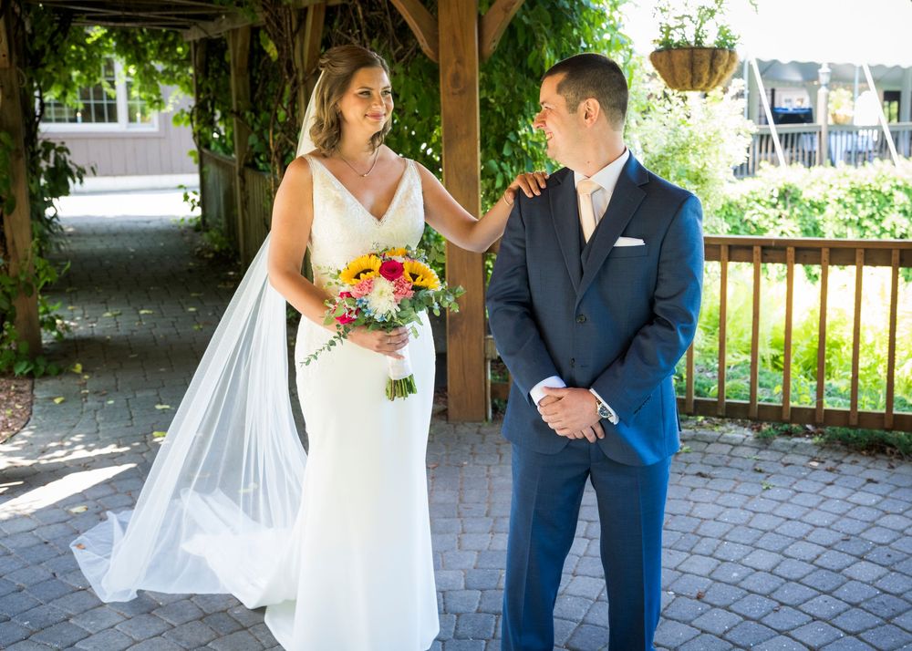 Bride in white gown with colorful bouquet touches groom's shoulder in blue suit during outdoor first look.