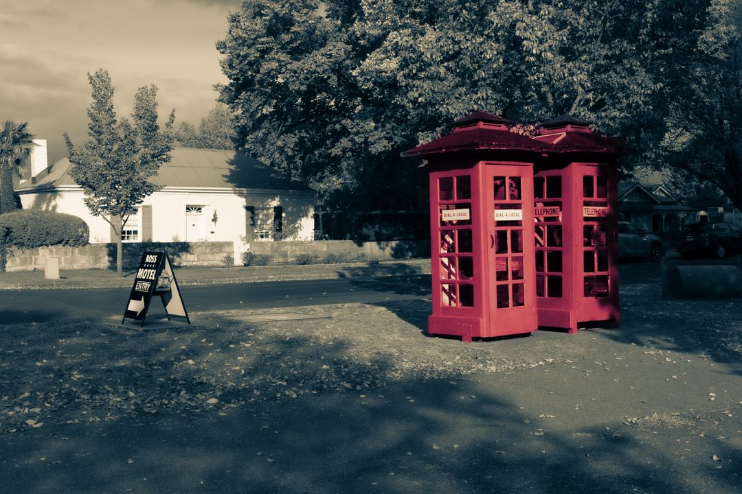 Vibrant red phone booth stands out in selective color photo among black and white trees.