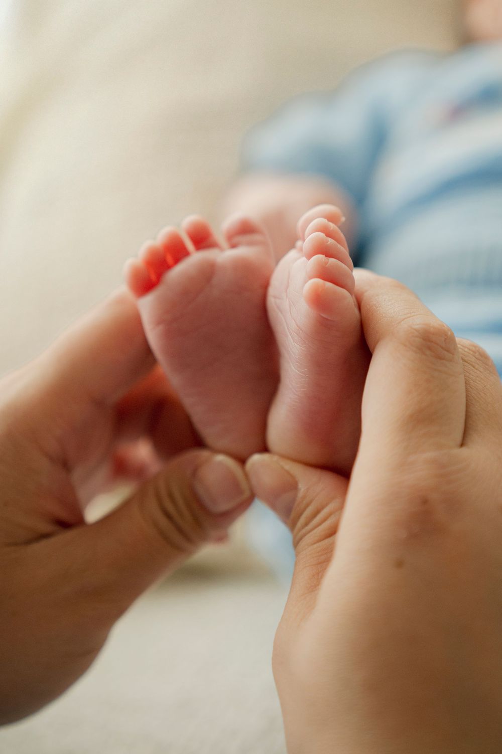 Close-up of adult hands gently holding tiny newborn baby feet, showcasing the delicate size difference.