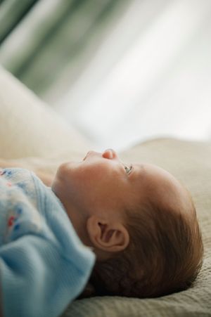 Peaceful newborn baby lying on back wrapped in a light blue swaddle blanket, eyes open, soft natural light.