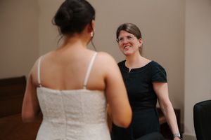A woman in black dress smiles emotionally at a bride in a white lace wedding gown during a first look moment.