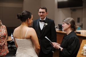 Couple exchanging vows before a judge in a courthouse wedding ceremony, groom in tuxedo, bride in white gown.