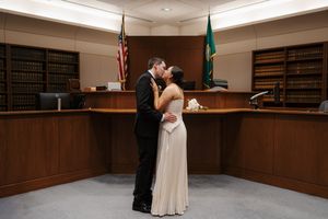 Couple sharing first kiss as newlyweds in a courthouse wedding ceremony with American and state flags.