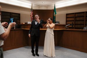 Joyful newlyweds celebrating after courthouse wedding ceremony, bride in white gown, groom in black tux.