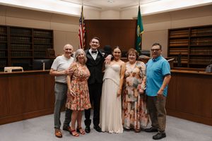 Six people pose together in a courtroom after a wedding ceremony, with the bride in white and groom in a suit.
