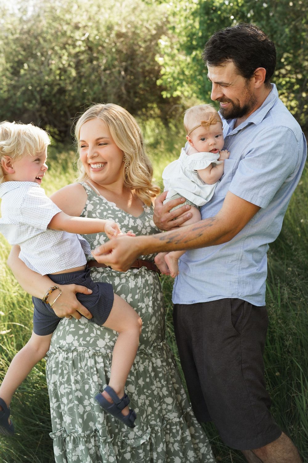 Happy family of four enjoying outdoor time, parents holding two young children in a green meadow.