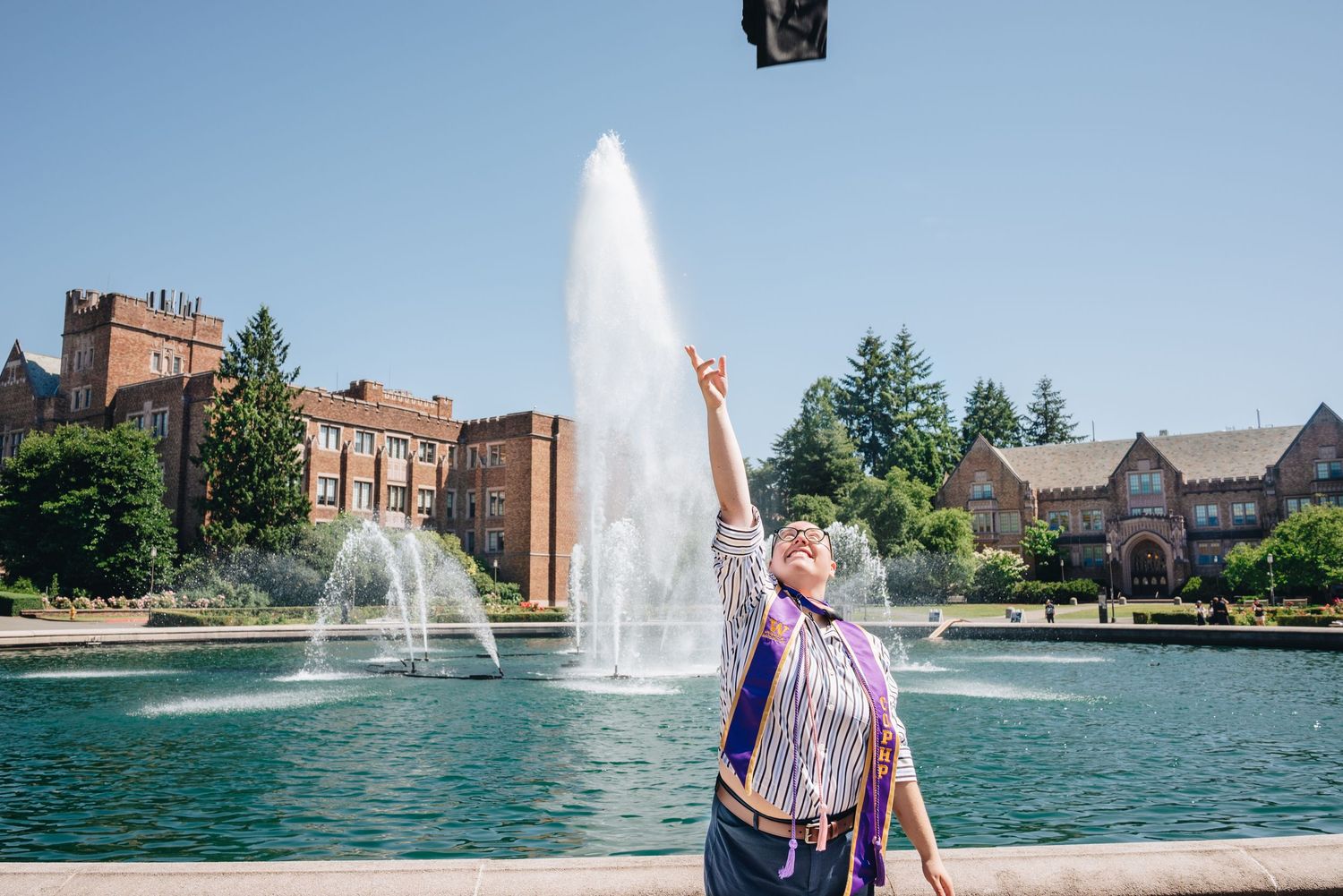 University of Washington graduate celebrating with a cap toss near Drumheller Fountain.