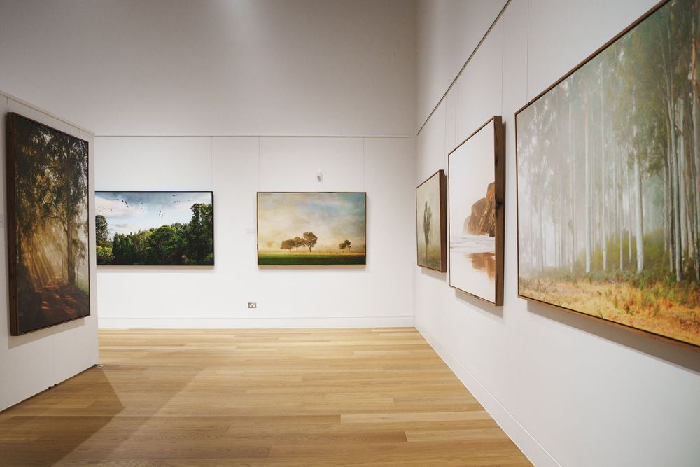 Serene art gallery displaying large-scale landscape paintings of trees and fields on white walls.