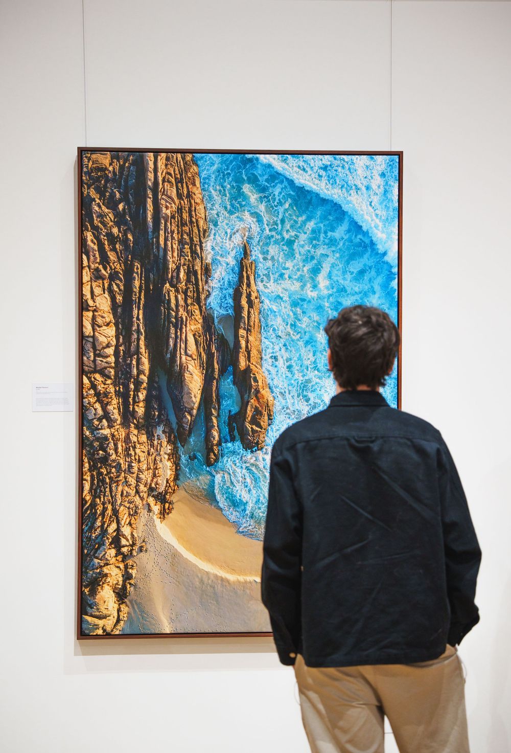 Person viewing stunning aerial coastal photography of rocky cliffs and turquoise ocean waves.
