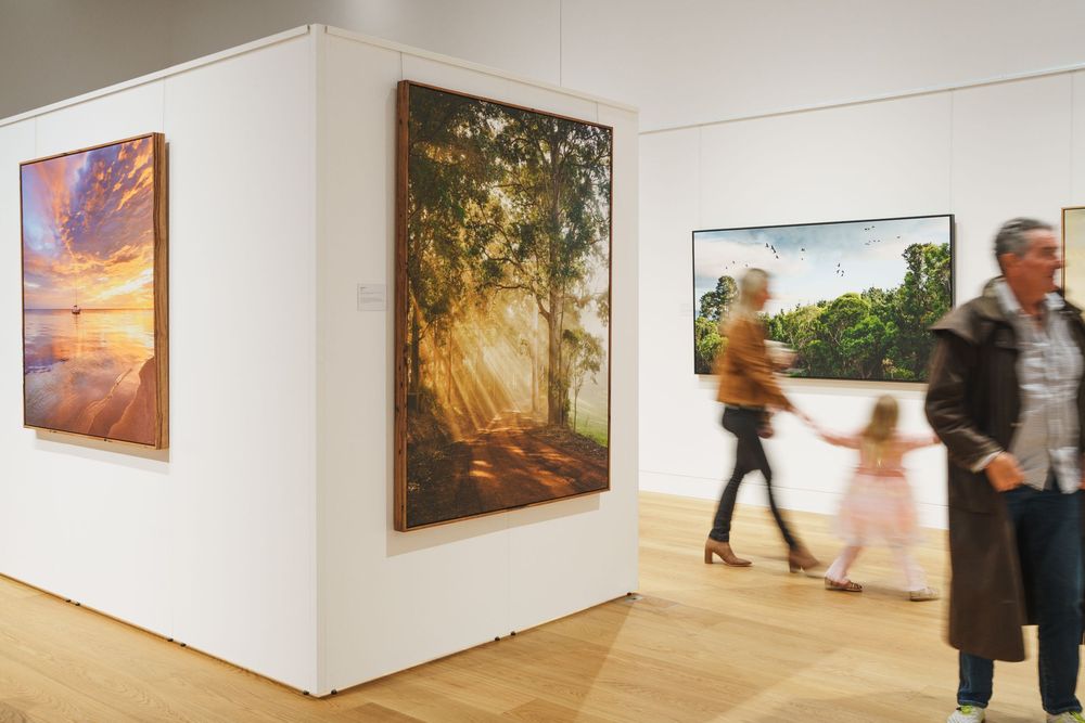 Visitors walking past large landscape photography prints in a modern art gallery.