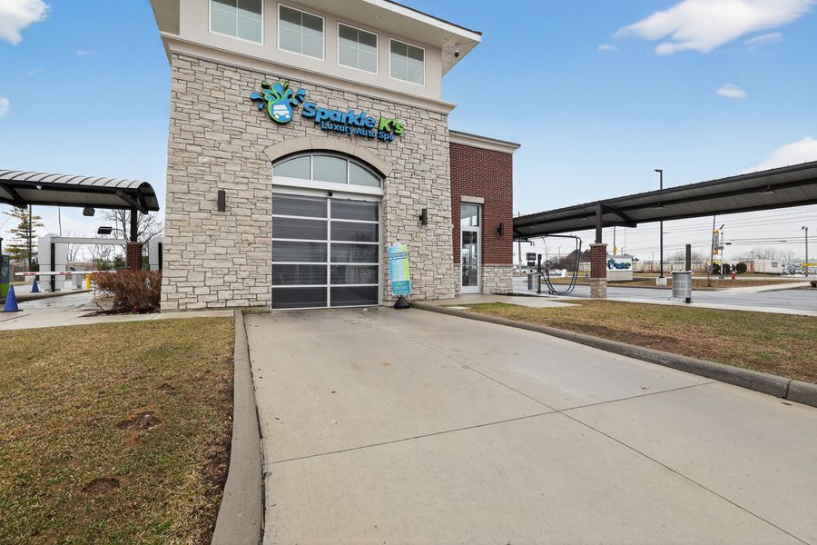 Contemporary car wash building with stone facade, glass garage door, and solar panel canopy structure.