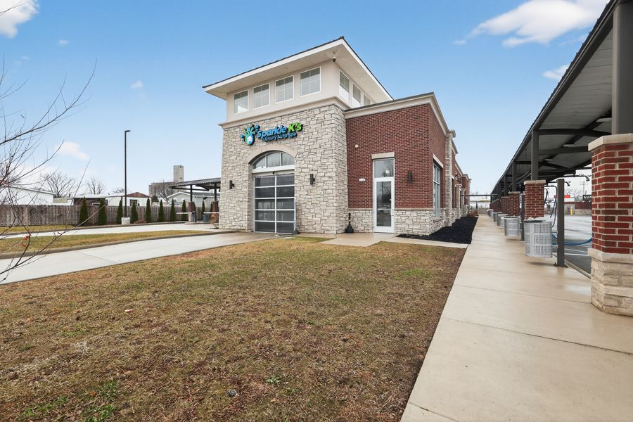 Modern brick and stone retail building with Prestige signage, sidewalk, and covered walkway on sunny day.