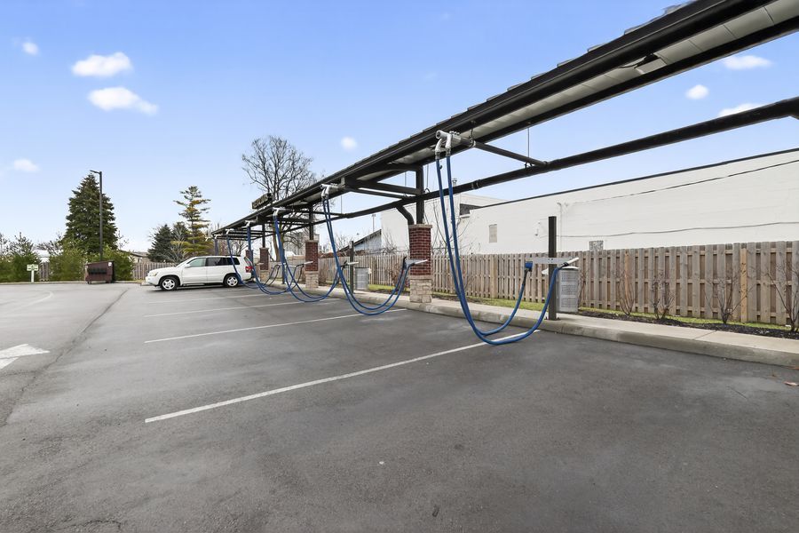 Outdoor parking lot with bike racks, solar panel canopy structure, wooden fence, and a white car under a partly cloudy sky.