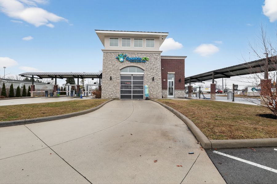Modern car wash facility with brick tower, covered wash bays, and curved driveway under a partly cloudy sky.
