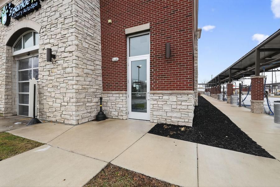 Exterior brick and stone wall of a car wash building with glass door entry and covered wash bays alongside.