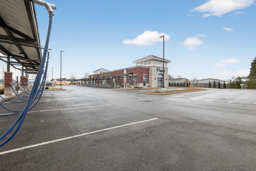 Spacious empty car wash parking lot with covered vacuum stations and brick building under blue sky.