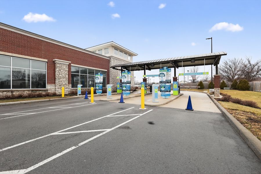 Car wash entrance with yellow bollards, blue cones, and covered tunnel entry at brick commercial building.