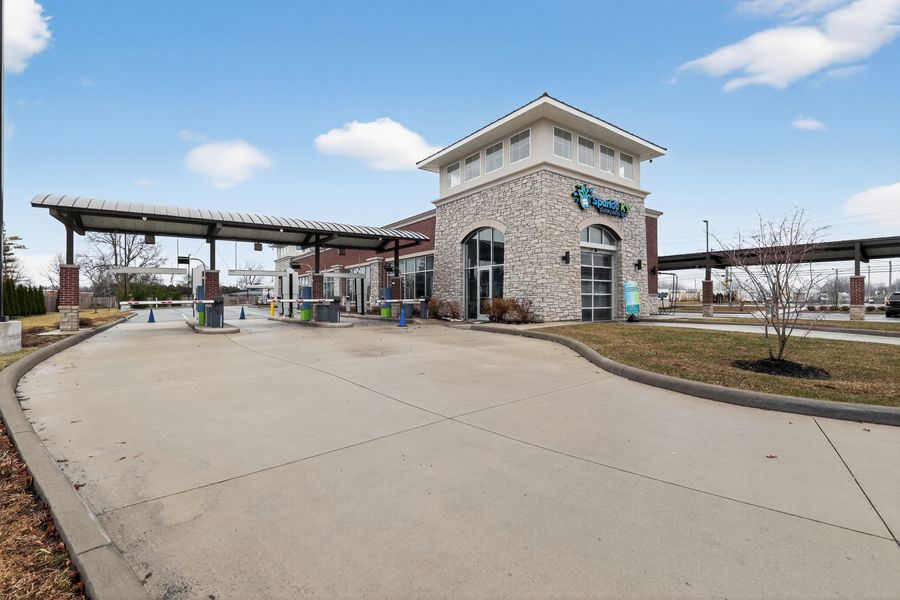 Modern car wash facility with stone tower, covered wash bay, and open concrete driveway on sunny day.