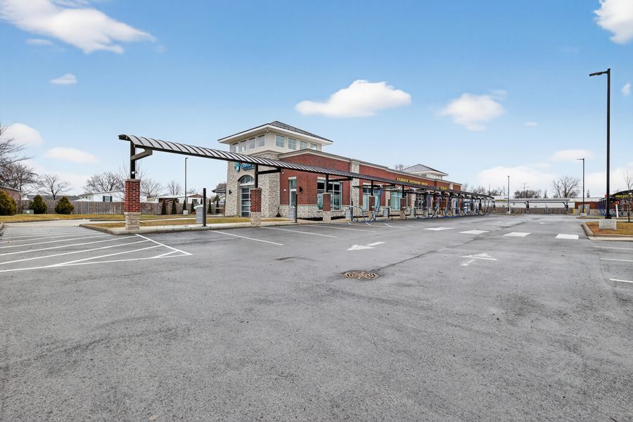 Spacious retail strip mall parking lot with brick shopping center and covered walkway under clear blue sky.