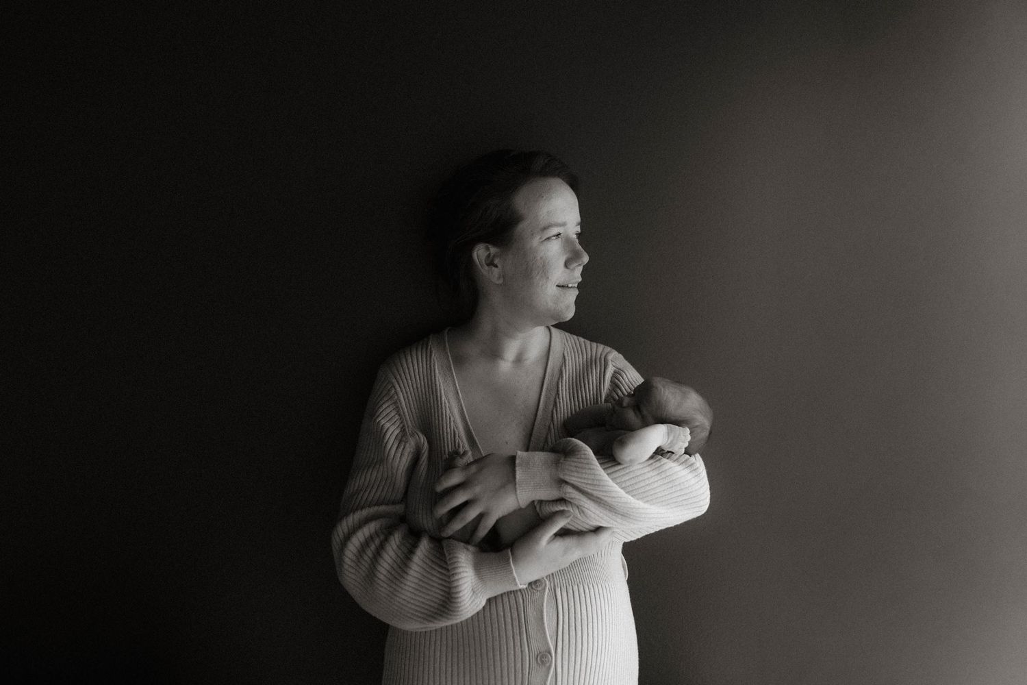Black and white photo of a mother tenderly holding her newborn baby against a dark background.