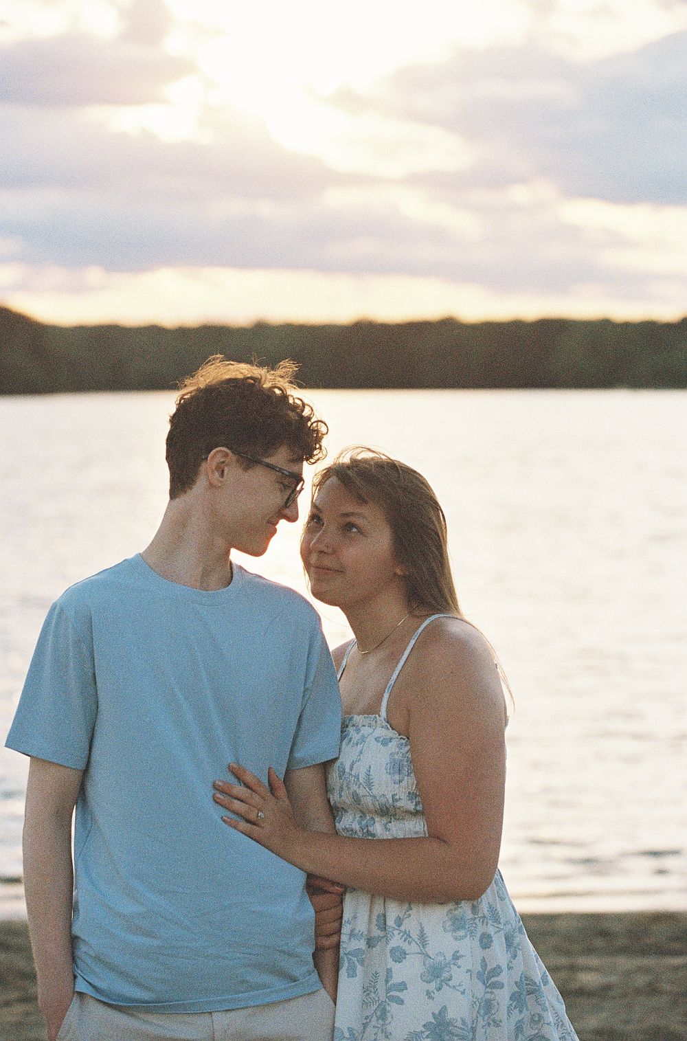 Young couple sharing a tender moment on a sandy beach at sunset with a lake backdrop.
