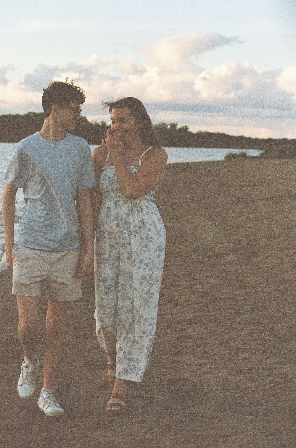 A couple walks hand in hand on a sandy beach at sunset, smiling and enjoying each other's company.