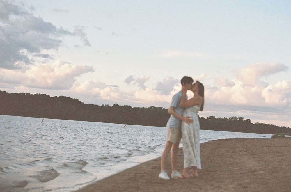 Couple kissing on a sandy beach shore at dusk with soft golden sunset light.