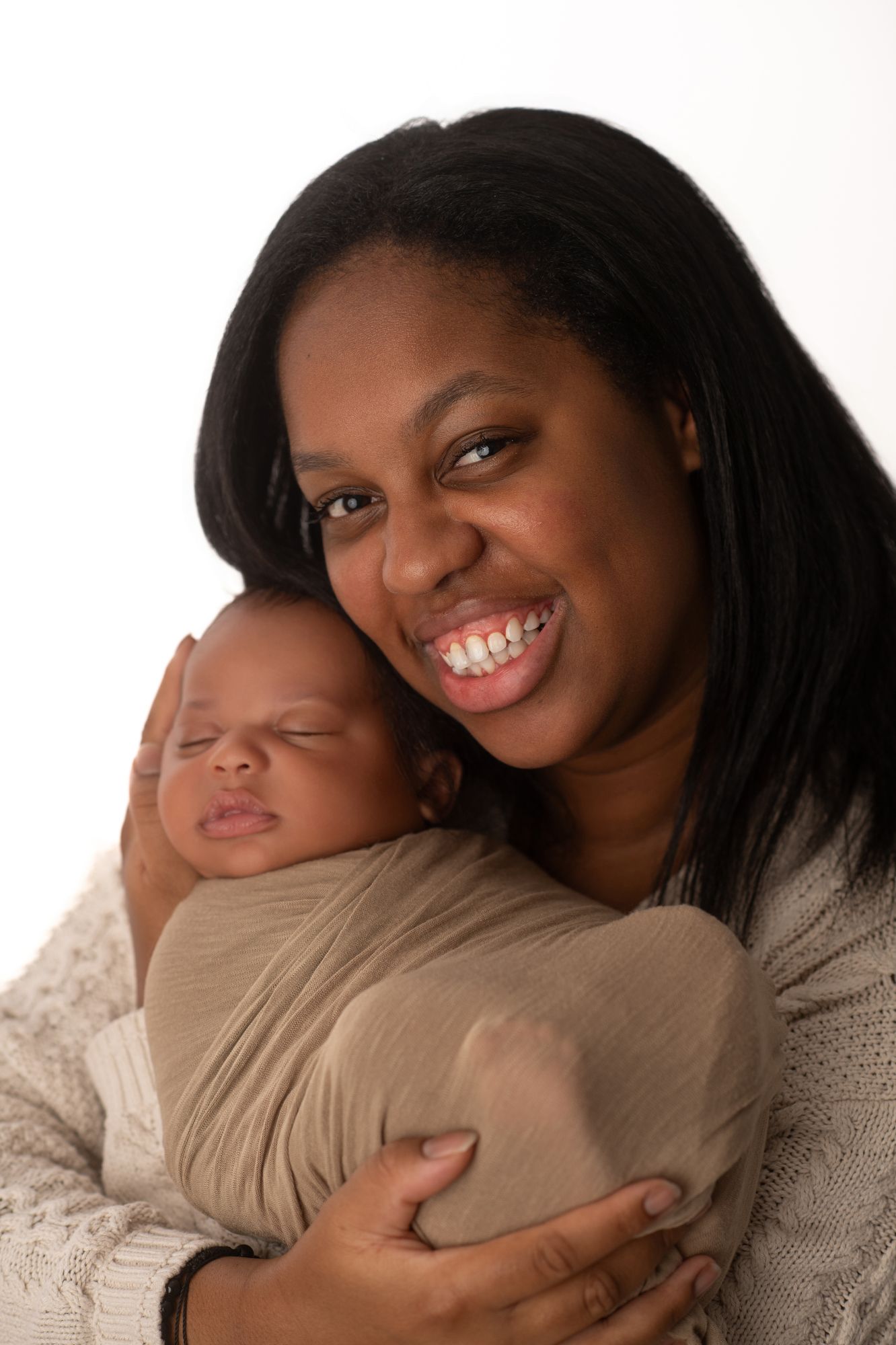 Smiling Black mother holding her swaddled newborn baby against a white background.
