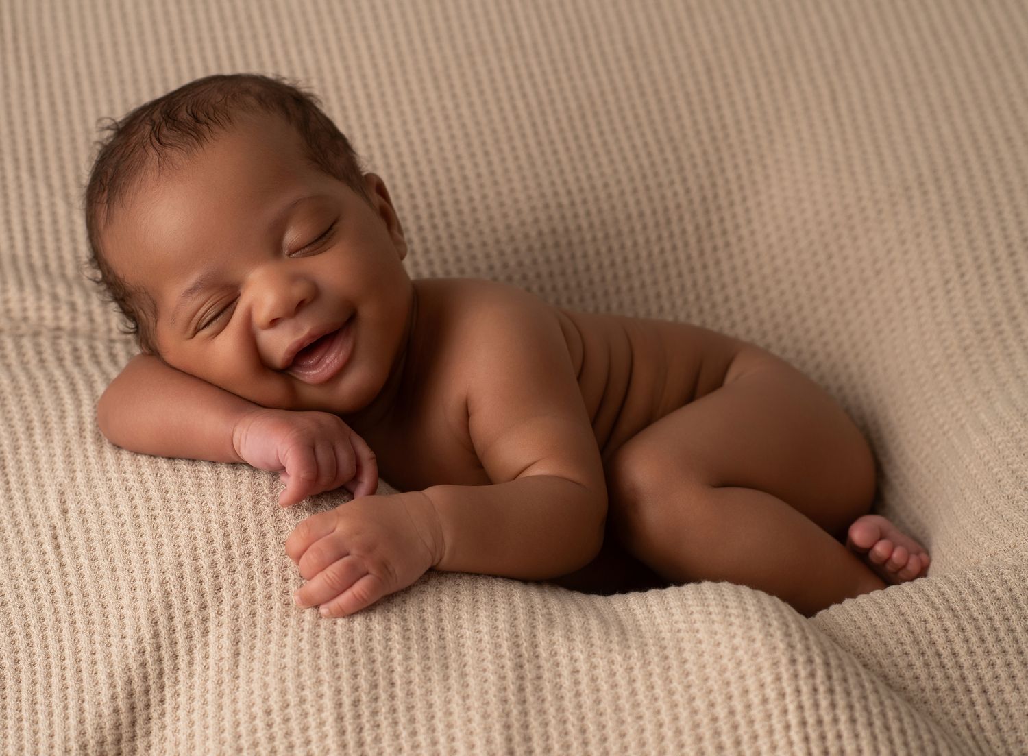 Smiling newborn baby lying on a soft cream textured blanket in a cozy posed newborn photography session.
