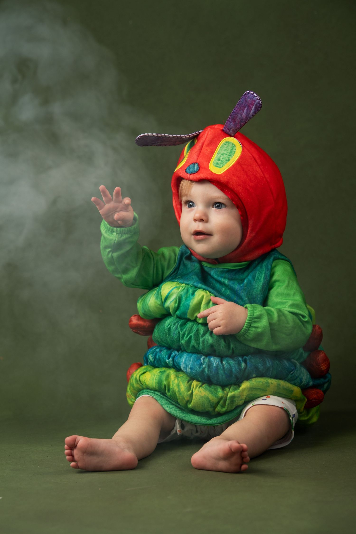 Baby wearing colorful Very Hungry Caterpillar Halloween costume sitting against green background.