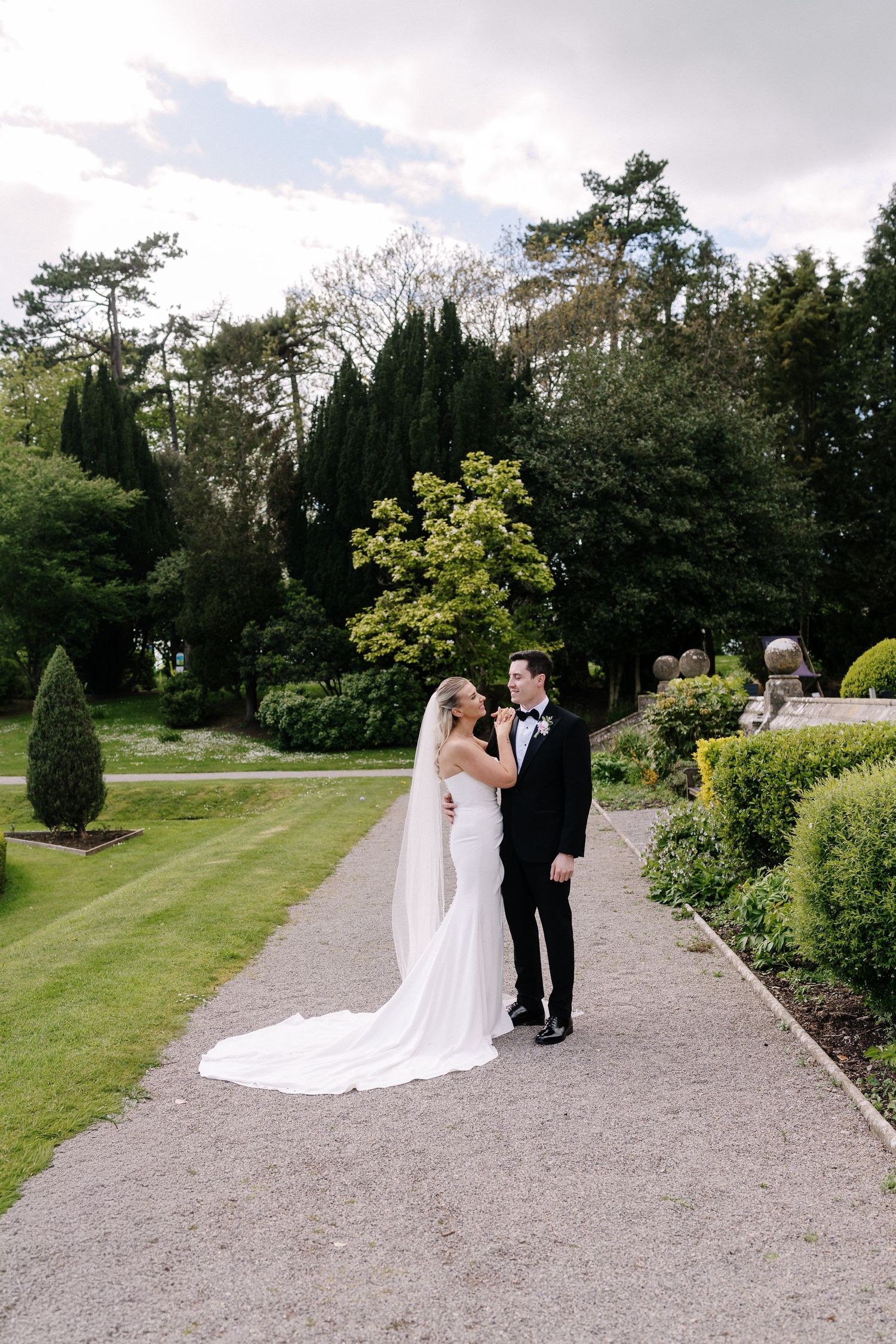 A bride and groom share a romantic moment on a garden path surrounded by lush greenery on their wedding day. Couple Shot's with Stu Tucker