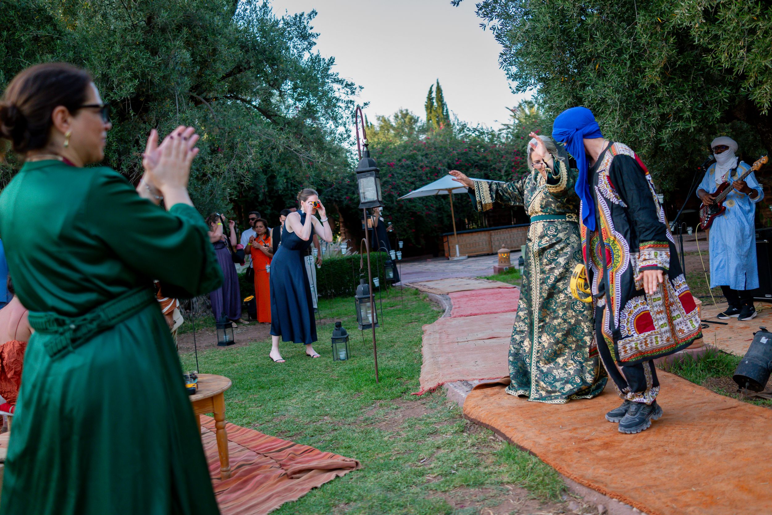 People in traditional Moroccan attire perform at an outdoor cultural ceremony with guests applauding in a garden setting.