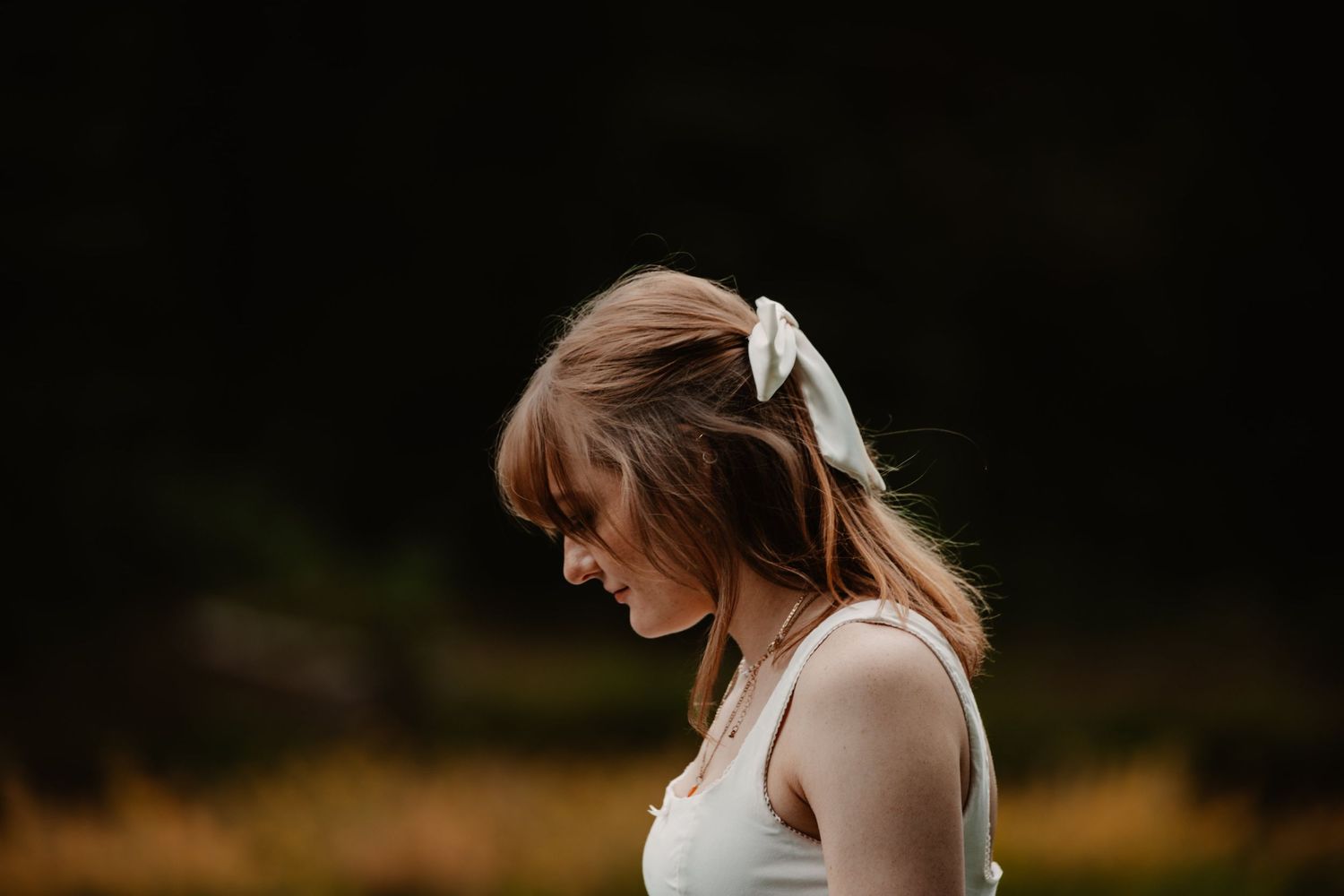A side profile captures a person in white with a bow hair accessory against a dark background.