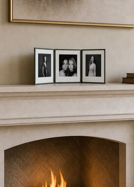Three black and white portrait photos displayed in frames on a elegant stone fireplace mantel with a warm fire burning below.