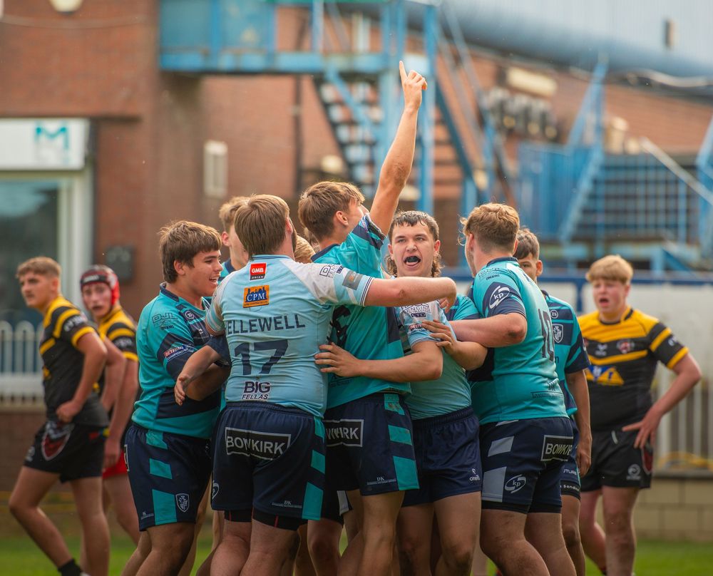 Rugby league players in teal jerseys celebrating together in a group huddle during a match.