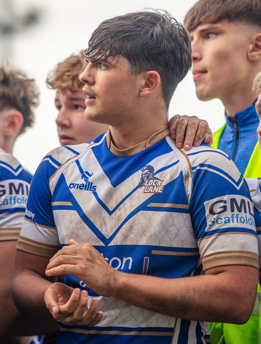 Young rugby league player in blue and white kit standing with teammates after a match.