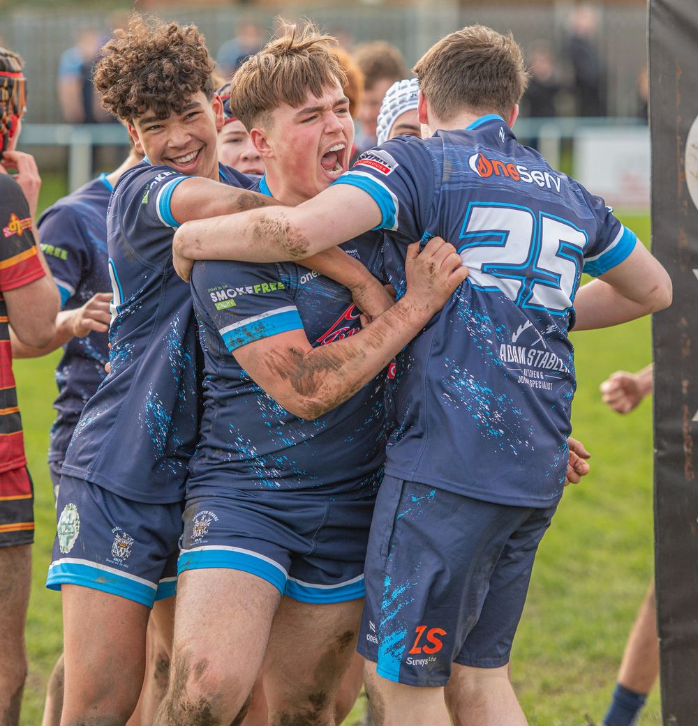 Young rugby league players celebrate together in muddy blue jerseys during an intense youth match.