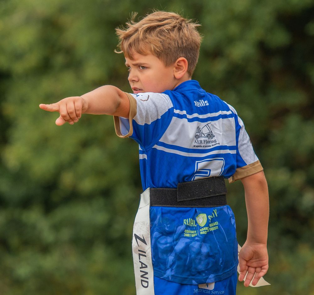 Young boy in blue rugby league kit pointing during a junior tag rugby match outdoors.