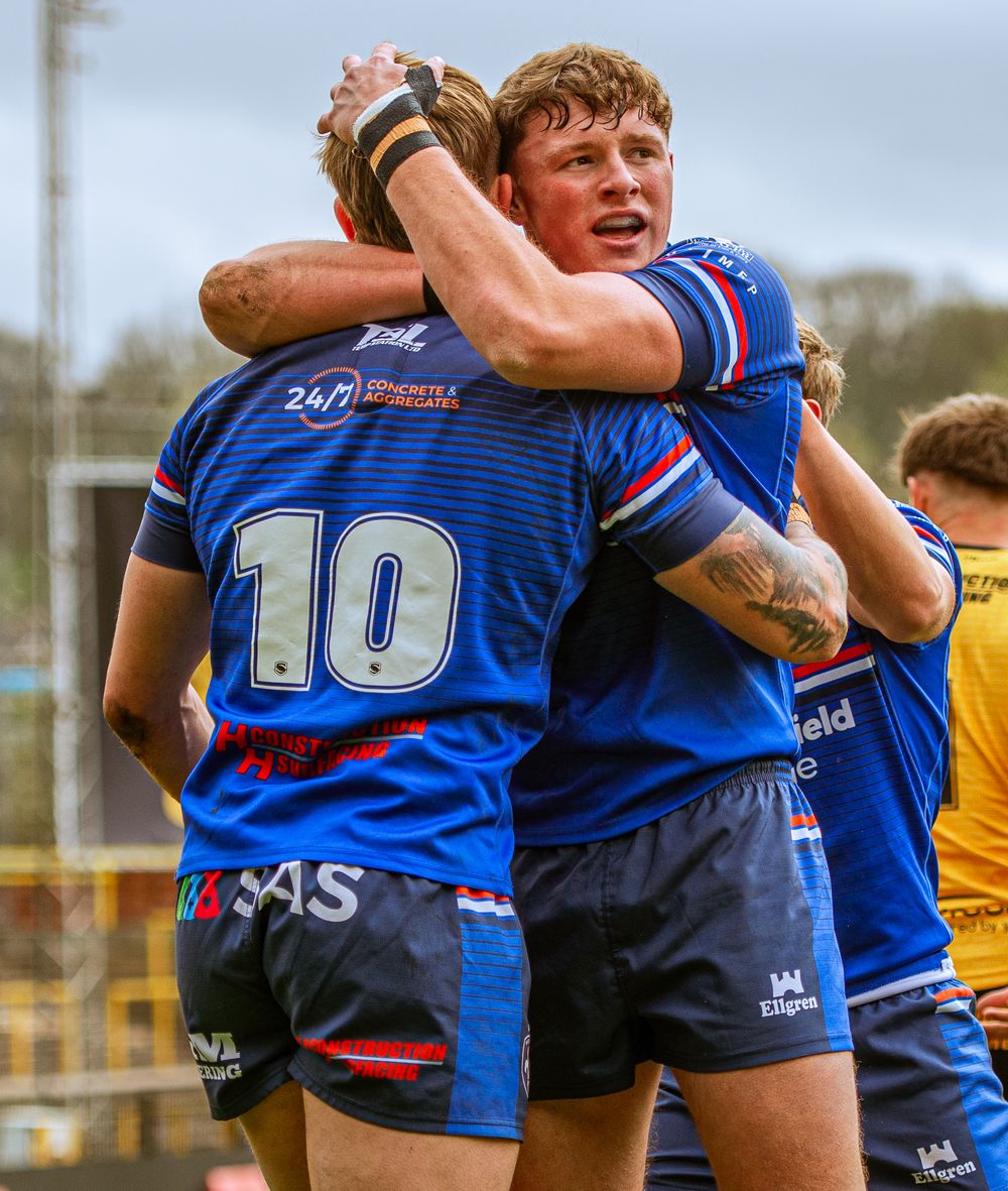 Two rugby league players in blue jerseys celebrate together on the field, with number 10 visible.