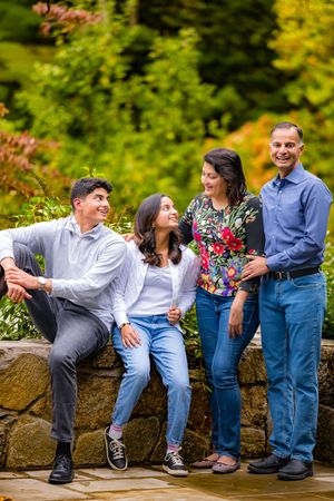 Family of four smiling and posing together outdoors in a lush green garden setting.
