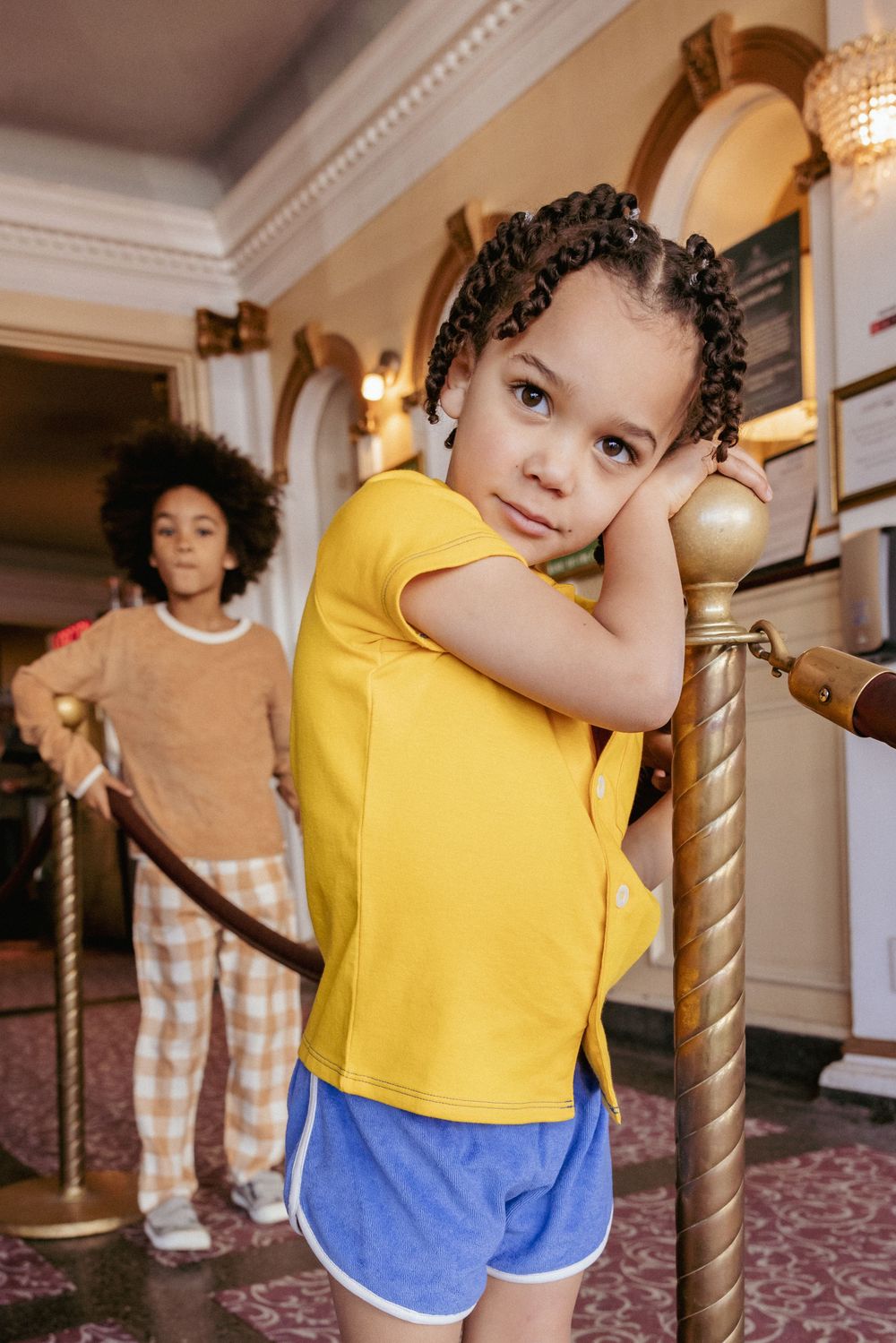 Young girl in yellow shirt leaning on a velvet rope stand in a theater lobby.