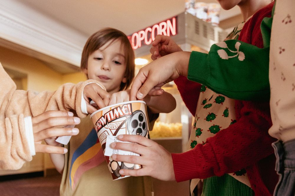 Children sharing popcorn at a movie theater concession stand.