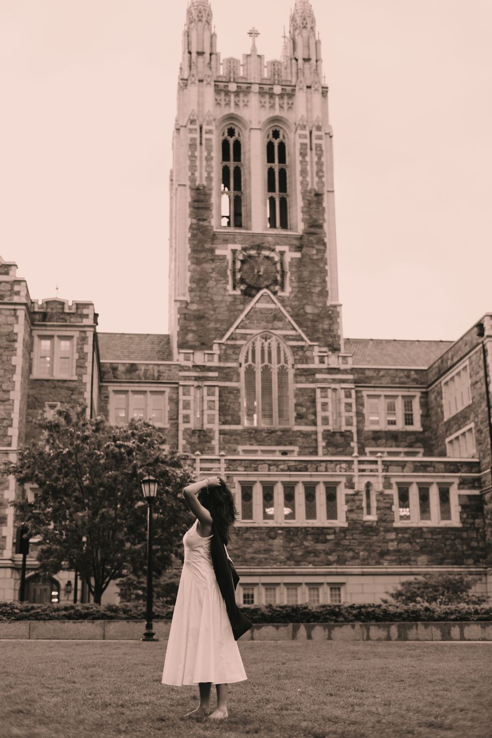 Boston college graduate facing away from camera looking towards a tall church bell tower on campus