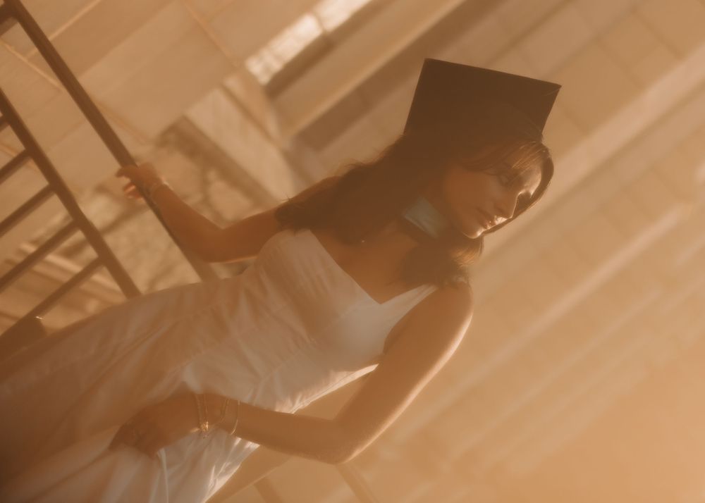 Candid photo of a Boston college graduate leaning against a railing on campus in a cinematic golden hour setting wearing cap & sash