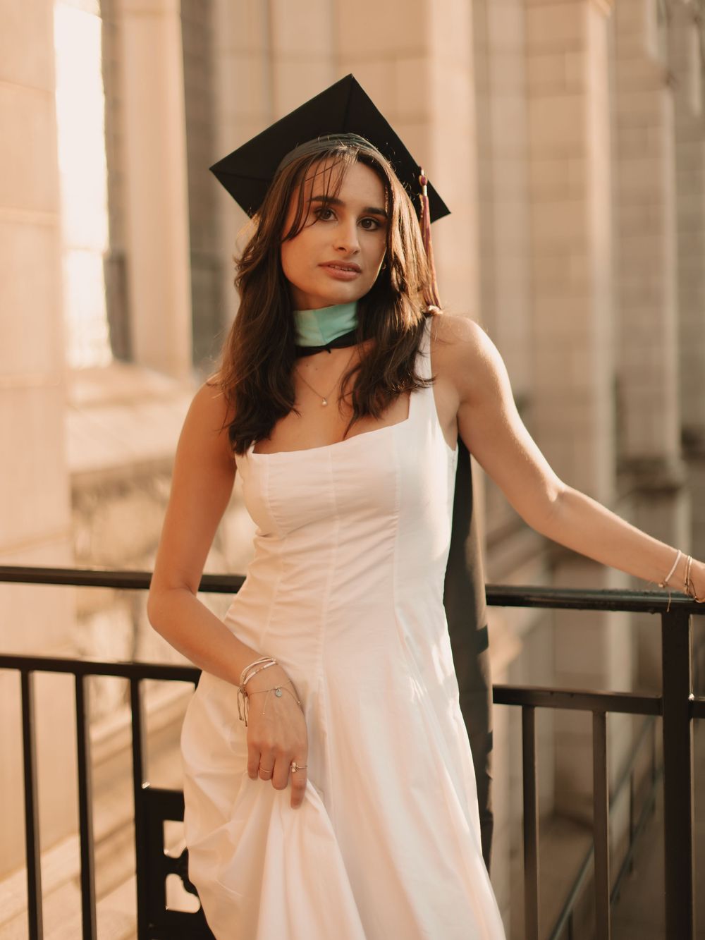 Boston college graduate leaning against a railing on campus in a cinematic golden hour setting wearing cap & sash