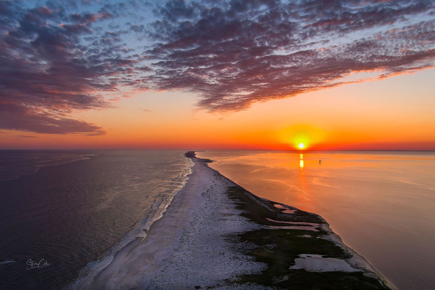 Aerial view of a narrow sandbar beach stretching into calm ocean waters at golden sunset, fine art photo by Steve Cole.