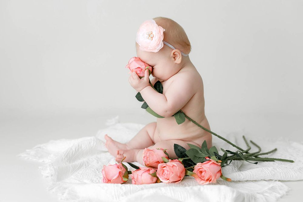 Baby girl smelling pink roses with floral headband on white background.