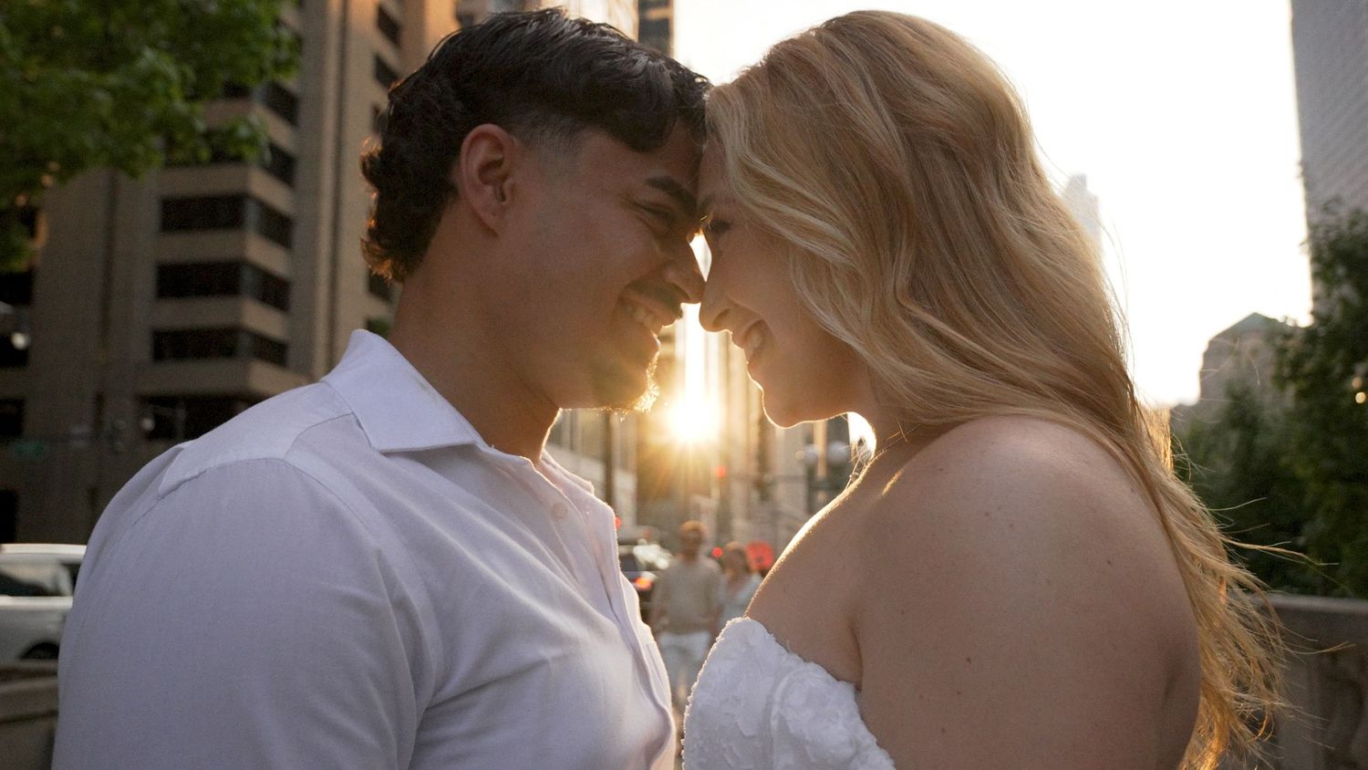A young couple with their foreheads touching and a reflection of the sunset in between them for an engagement session video