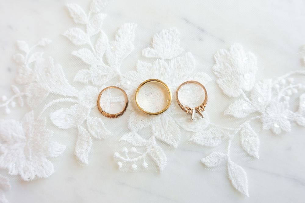 Three gold wedding rings displayed on white lace fabric, including a diamond engagement ring.